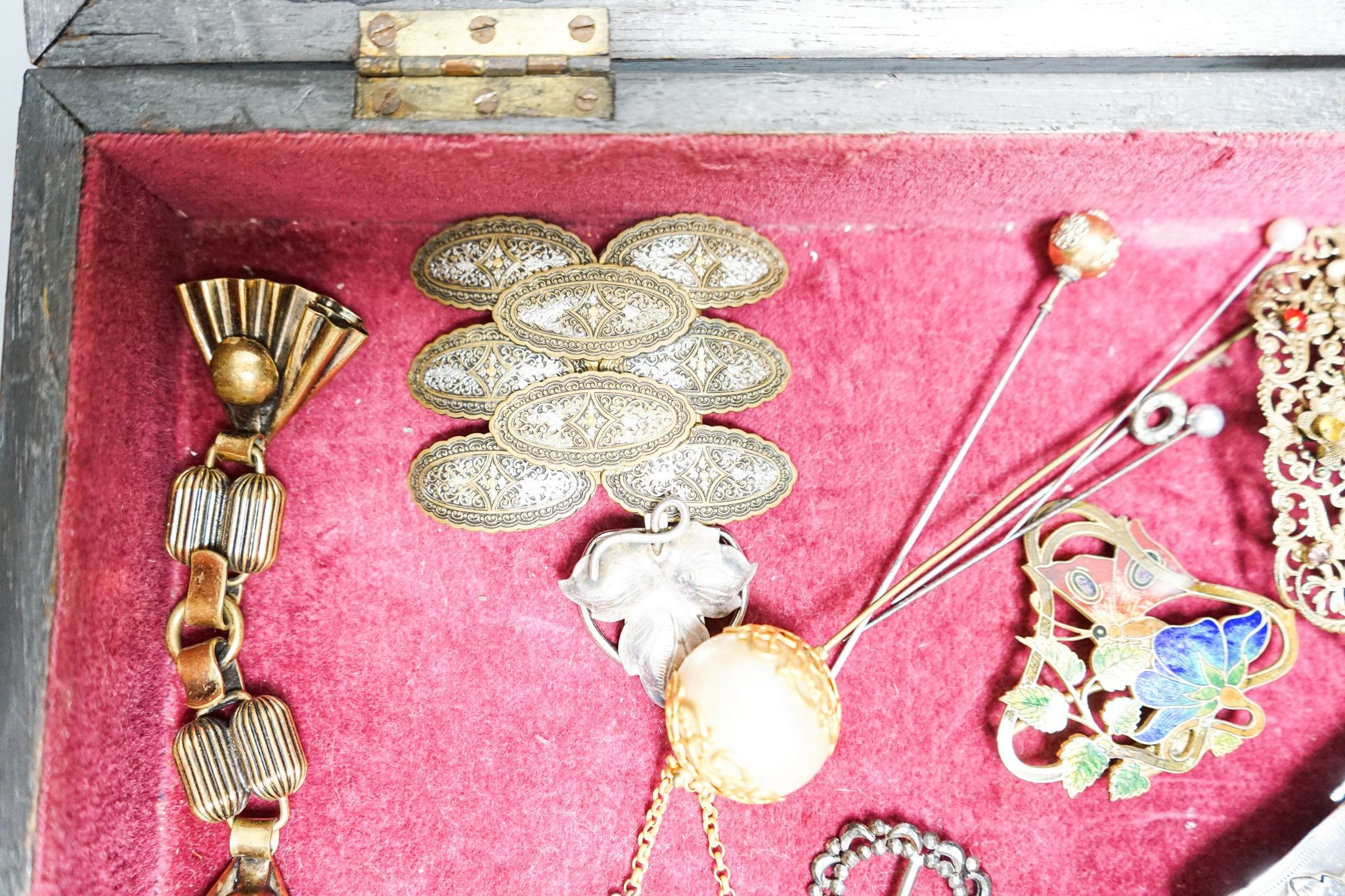 A group of belt buckles, clips and hatpins in a mahogany display case, 30.5cm